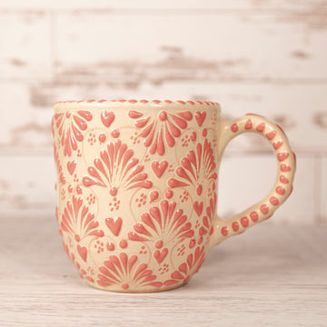 A beige ceramic mug with red floral patterns and a handle on a wooden surface.