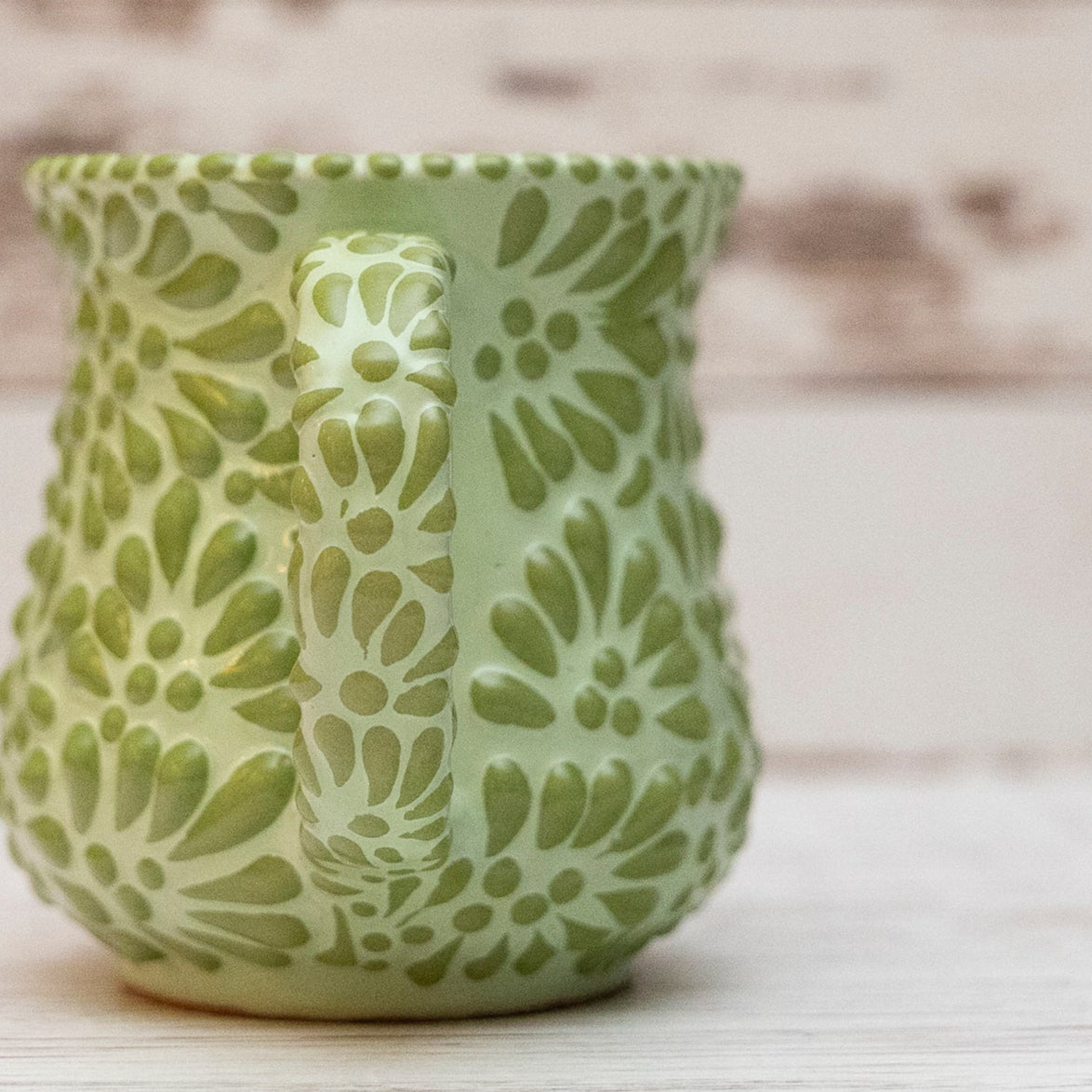 Green ceramic mug with floral patterns on a wooden surface and background