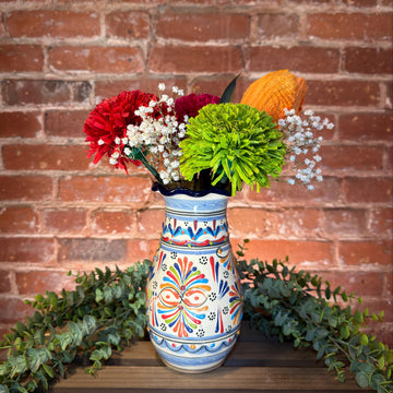 Decorative vase with colorful patterns filled with flowers against a brick wall.