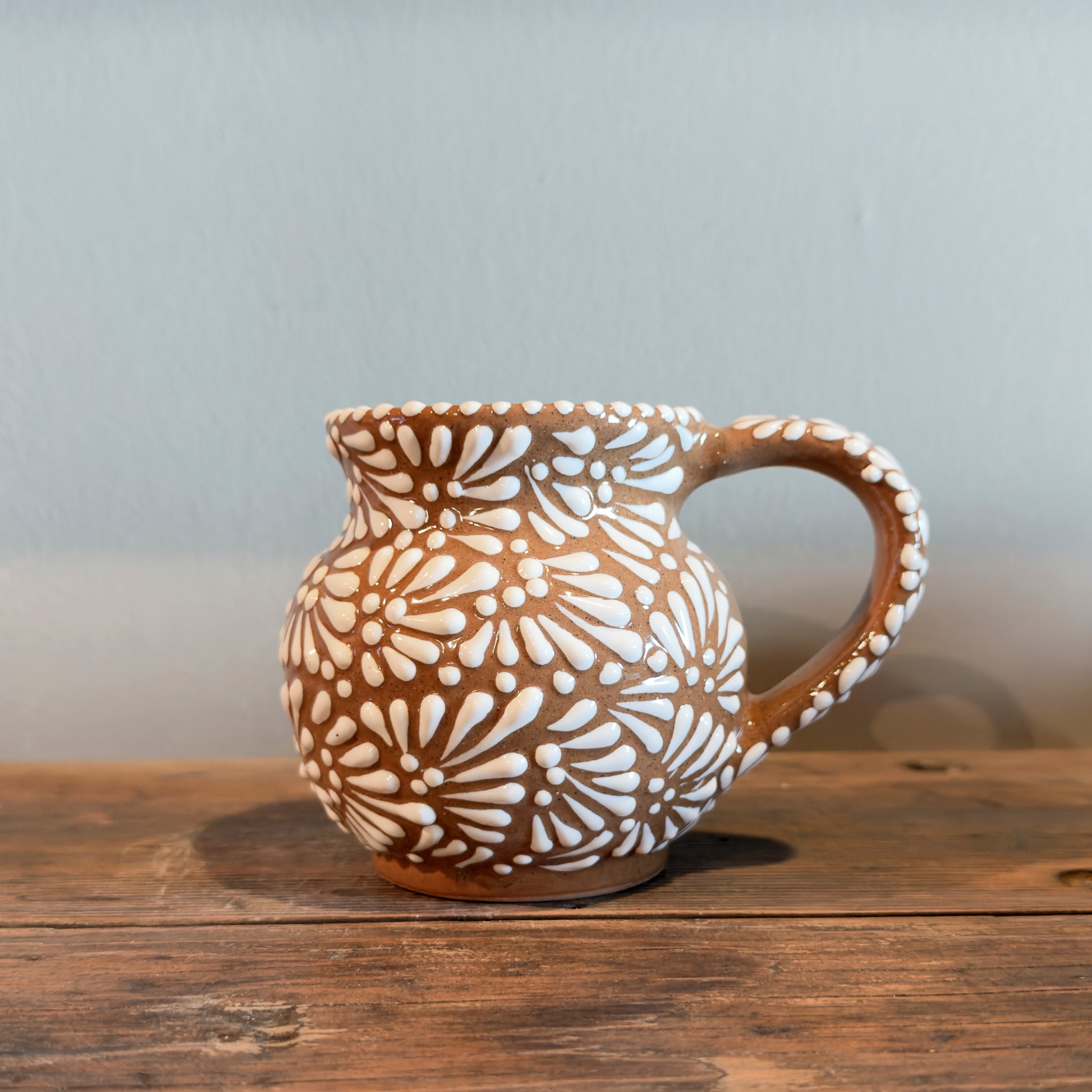 Ceramic pitcher with white floral patterns on a wooden surface
