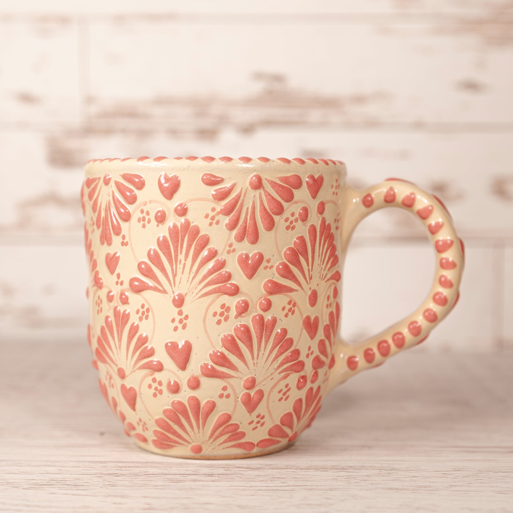 A beige ceramic mug with red floral patterns and a handle on a wooden surface.