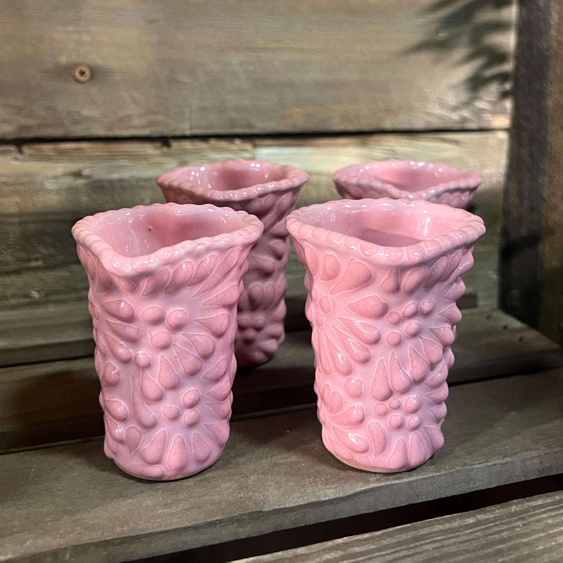 Set of four pink textured shot glasses on a wooden surface with a wooden background